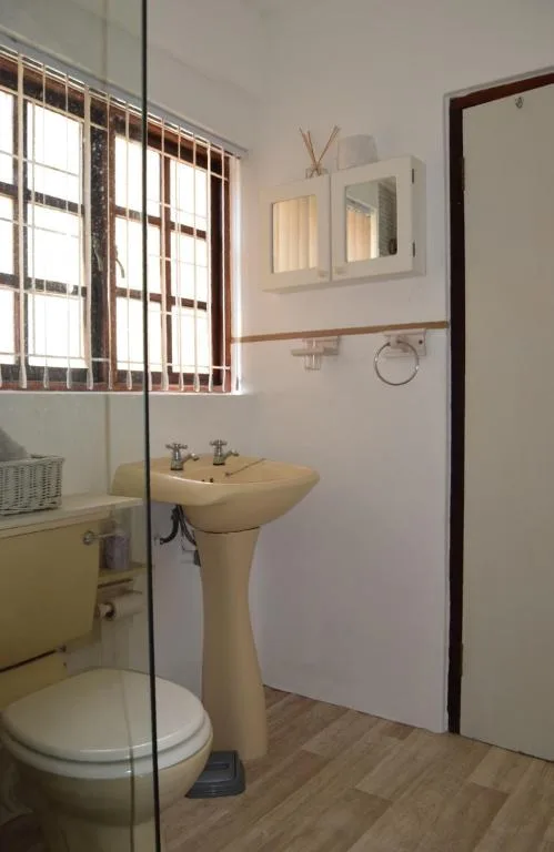 Clean bathroom with pedestal sink, toilet, and window with security bars