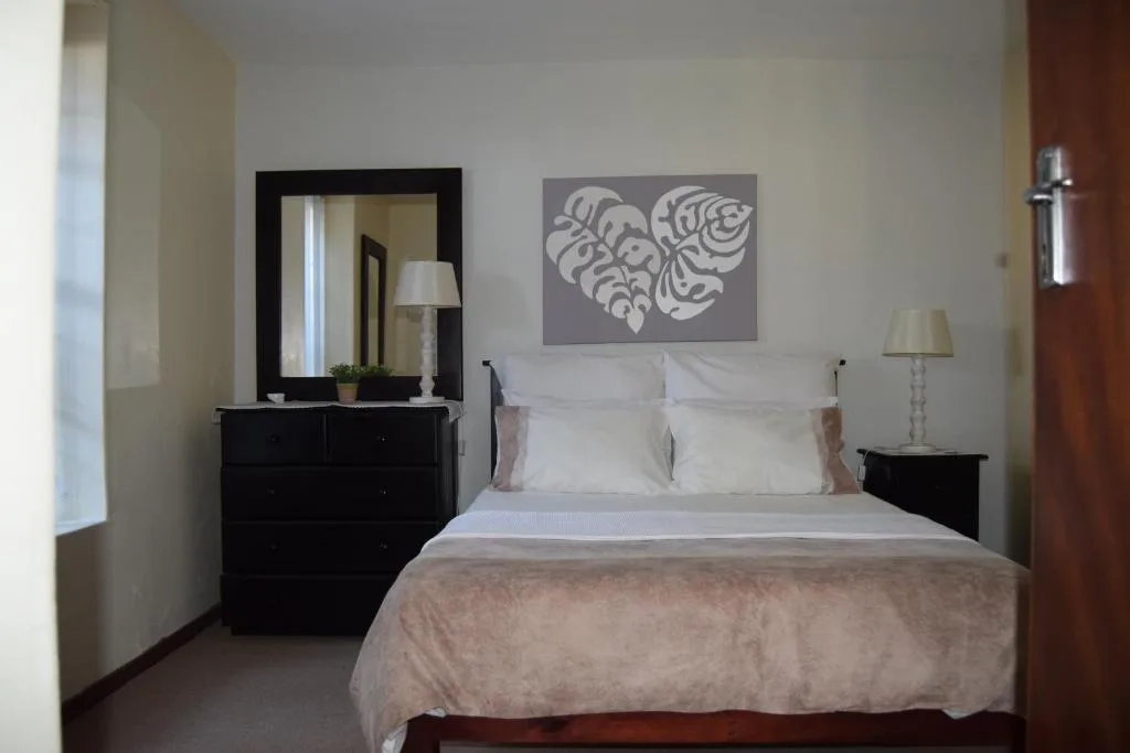 Bright bedroom with queen bed, black dresser, and modern leaf artwork