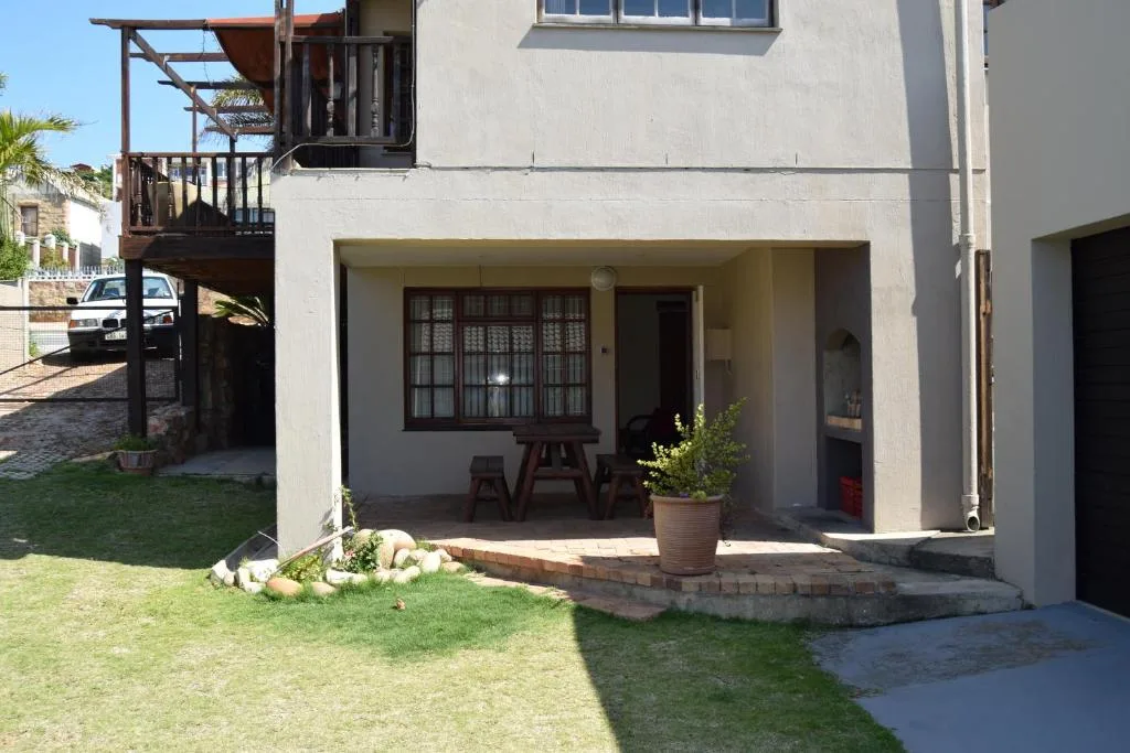Modern apartment exterior with covered patio, garden, and wooden deck stairs
