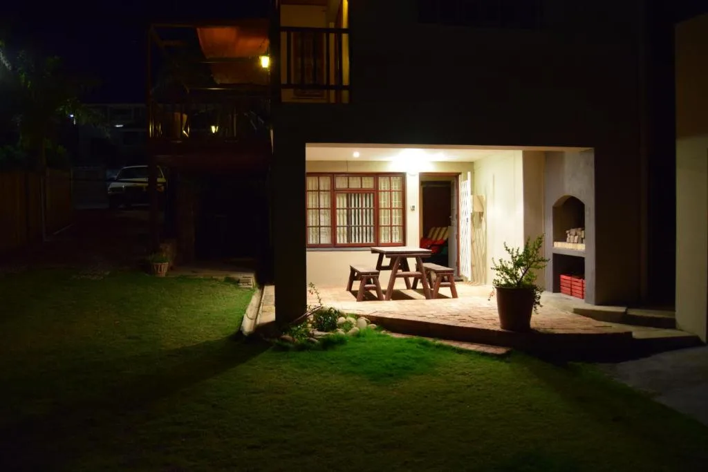 Night view of property entrance with illuminated patio and wooden furniture
