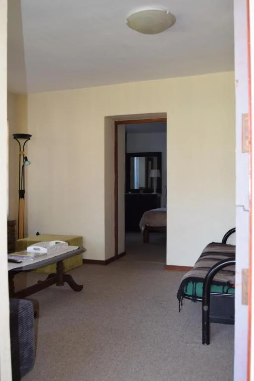 Spacious living room with cream walls, standing lamp, and doorway to bedroom