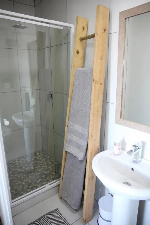 Modern bathroom with enclosed shower, pedestal sink, and wooden towel rack