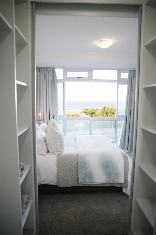 Bright bedroom with bed and expansive windows overlooking coastal bay view