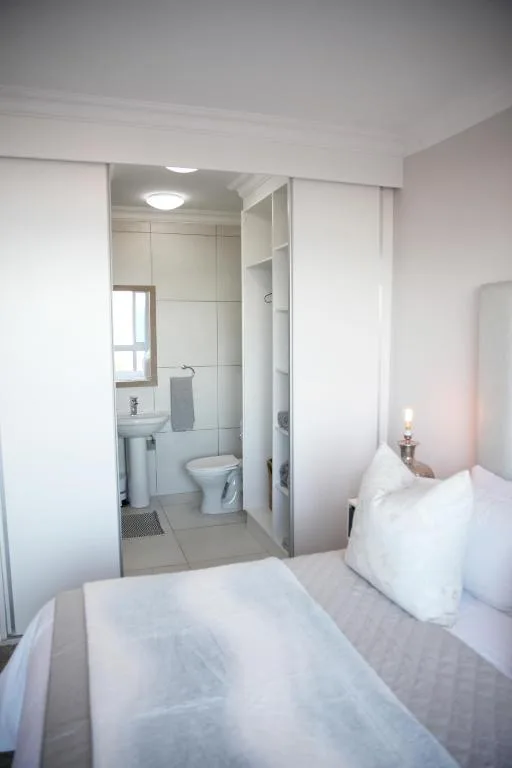 Bright bedroom with white bedding and ensuite bathroom visible through open door