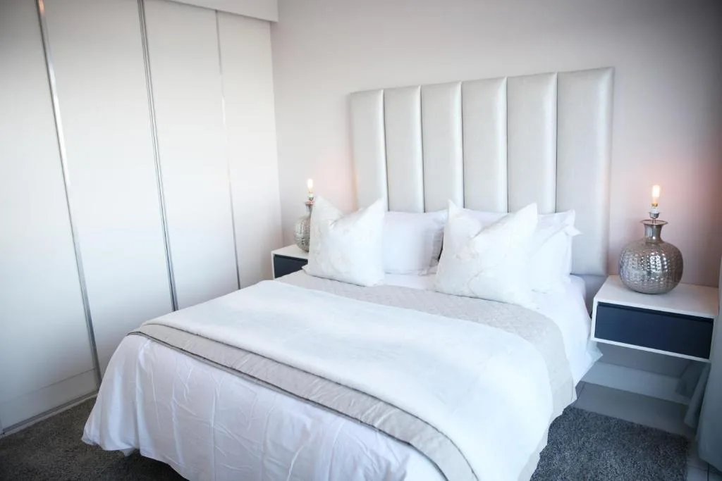 Modern bedroom with white bedding, padded headboard, and bedside candles