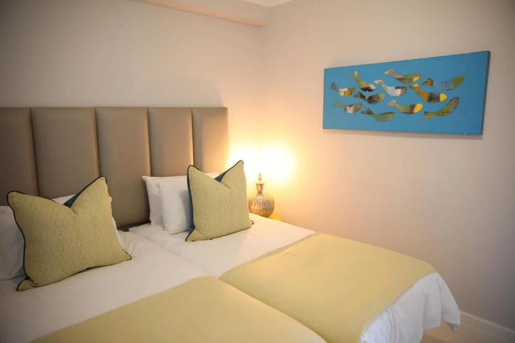 Bright bedroom with twin beds, yellow cushions, padded headboard, coastal artwork