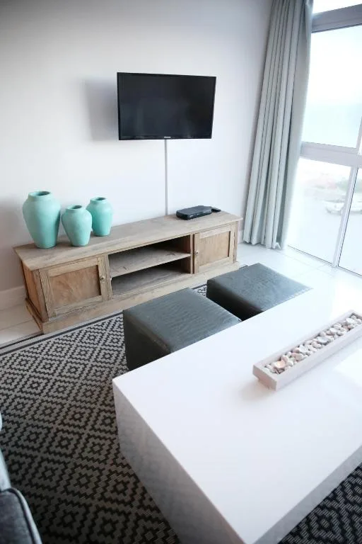 Modern lounge with wall-mounted TV, wooden media console, and coastal views
