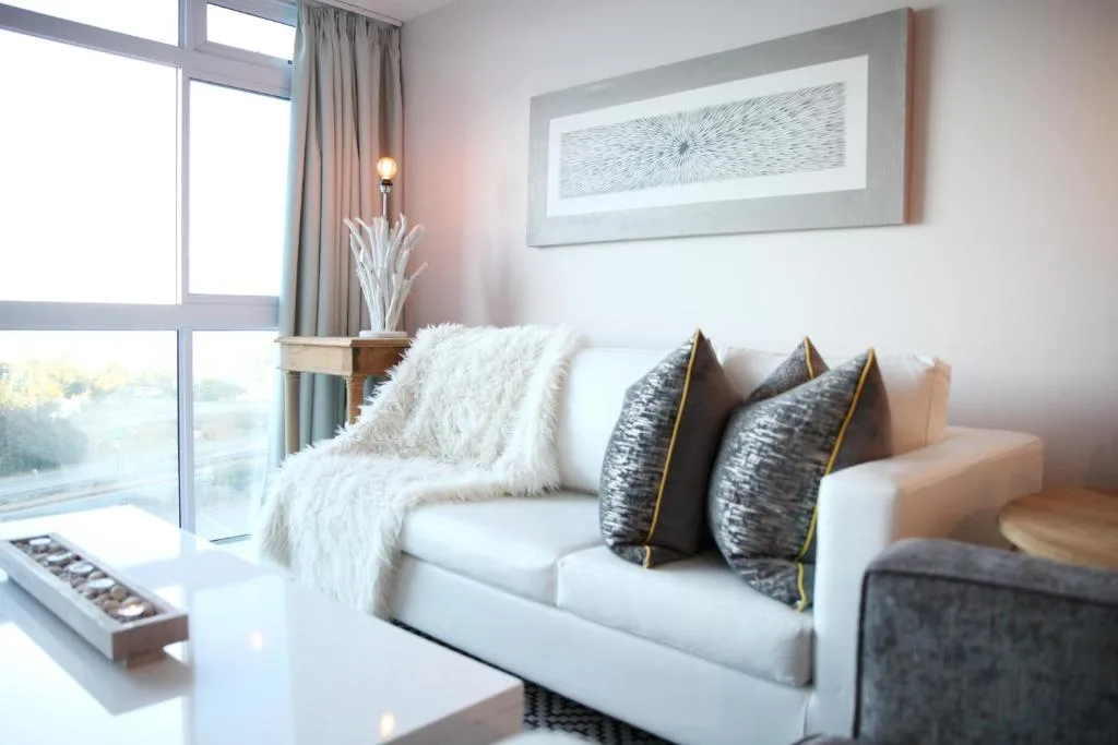 Modern lounge with white sofa, patterned cushions, large windows overlooking bay