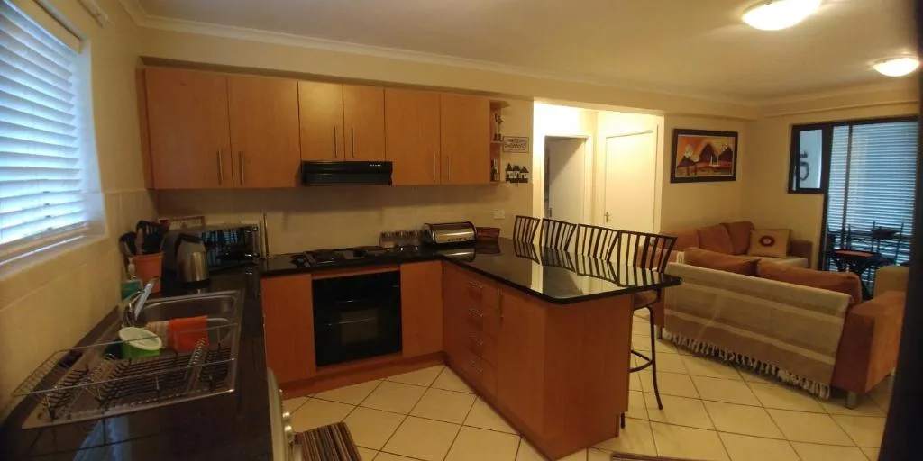 Open-plan kitchen with orange cabinetry, black countertop, and adjacent lounge seating area