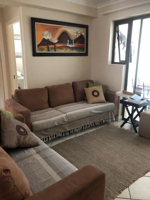 Cozy lounge with brown sofa, armchair, framed artwork, and garden views
