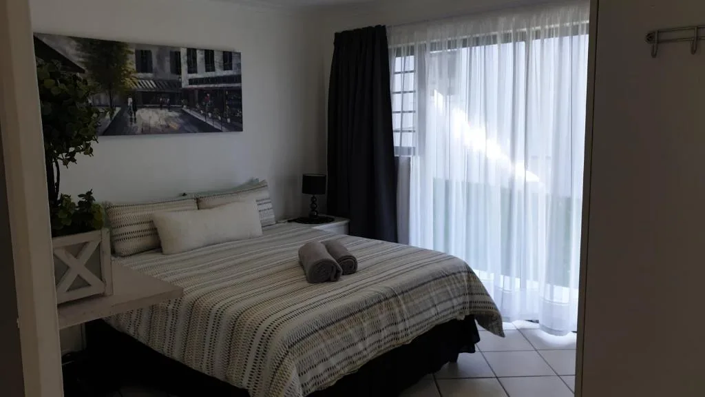 Bright bedroom with striped bedding and large windows overlooking gardens
