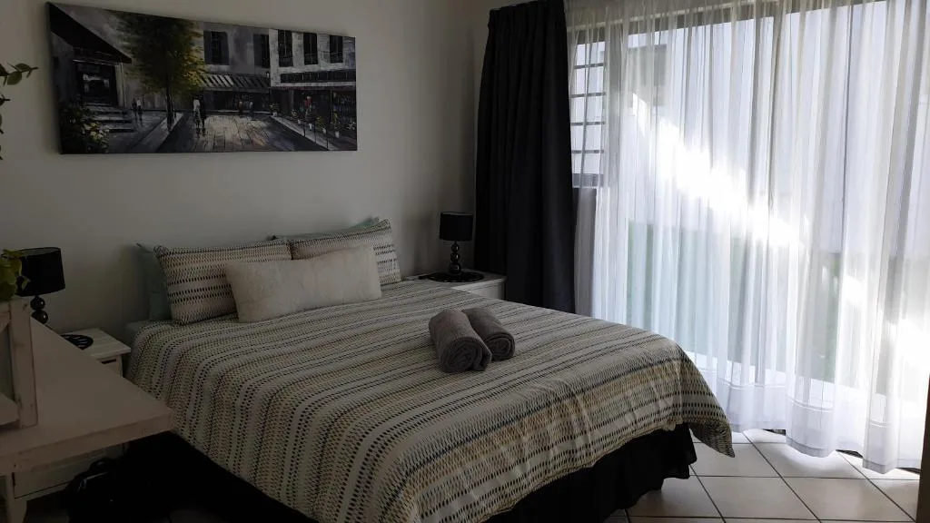 Bright bedroom with queen bed, patterned bedding, and sheer curtains allowing natural light