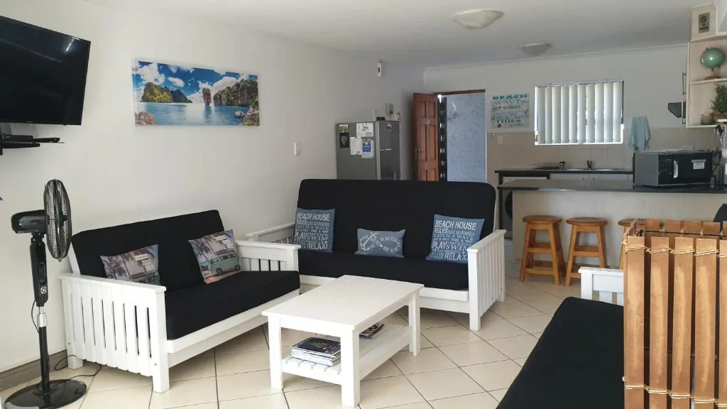 Open-plan lounge with black and white sofas, TV, and kitchen visible