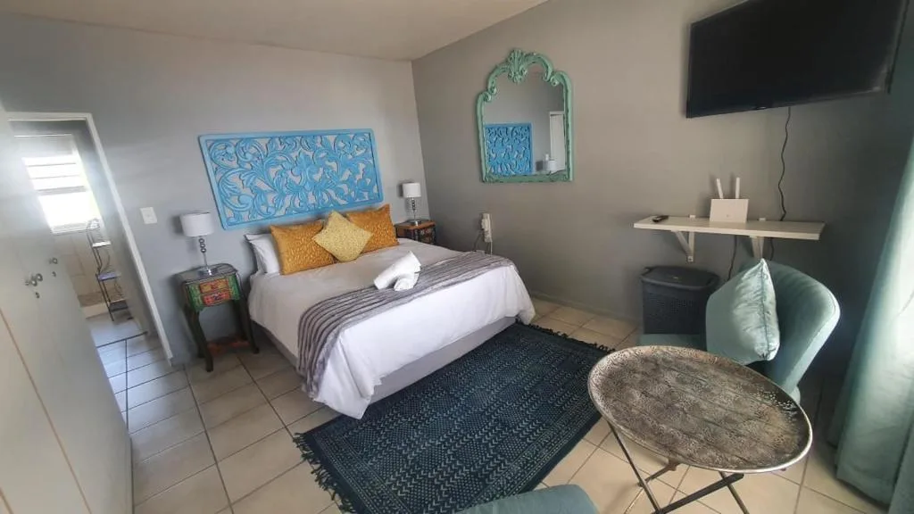Bright bedroom with queen bed, turquoise artwork, wall-mounted TV, and seating area