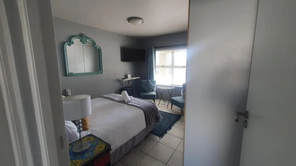 Bright bedroom with queen bed, turquoise mirror, and lounge seating area