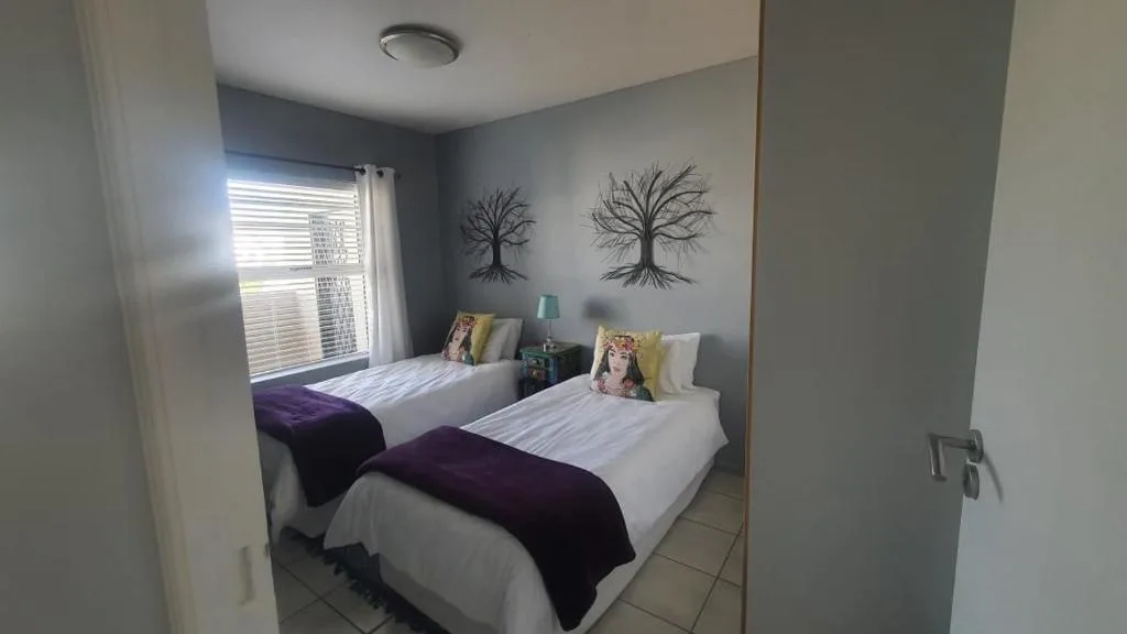 Twin bedroom with white linens, purple throws, and decorative tree artwork