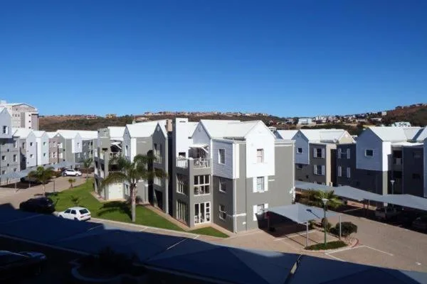 Modern apartment complex with white and navy facades, landscaped grounds, clear sky