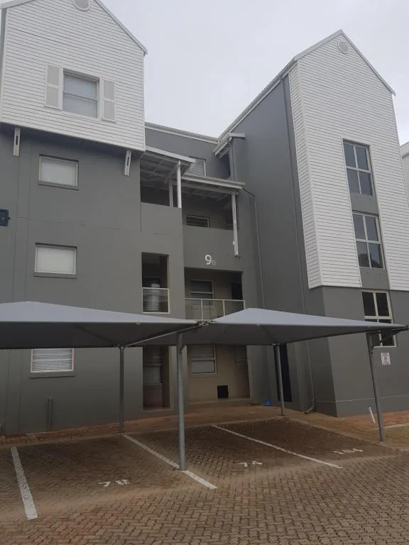 Modern multi-story apartment building with gray and white cladding, covered carport