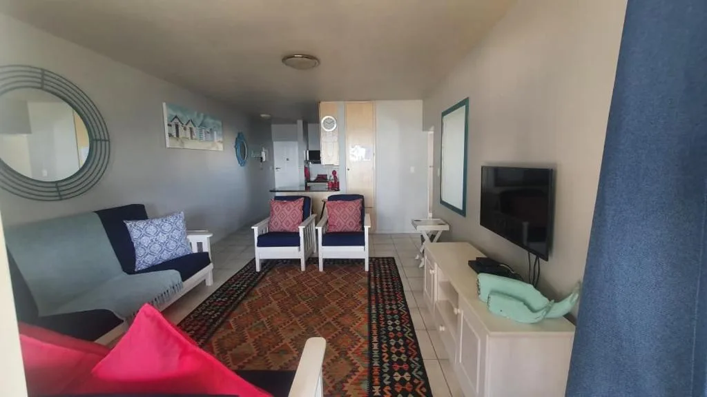 Open-plan lounge with sofa, armchairs, TV, and kitchen area visible