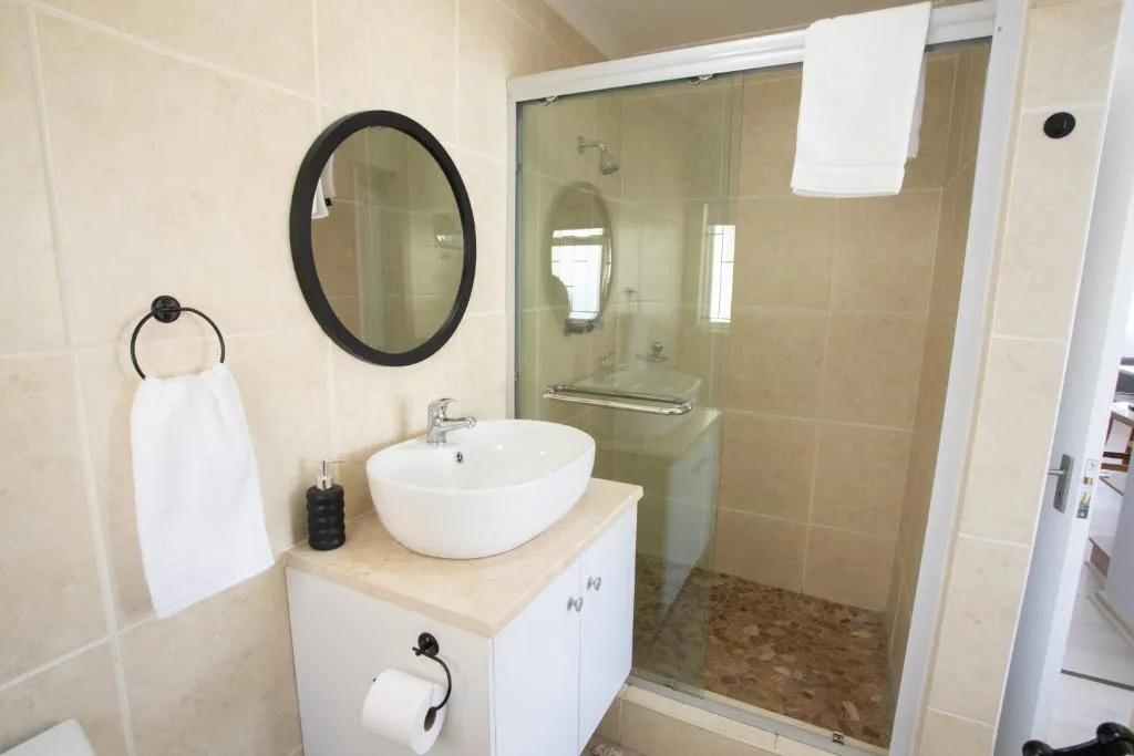 Modern bathroom with round mirror, vessel sink, and walk-in shower enclosure