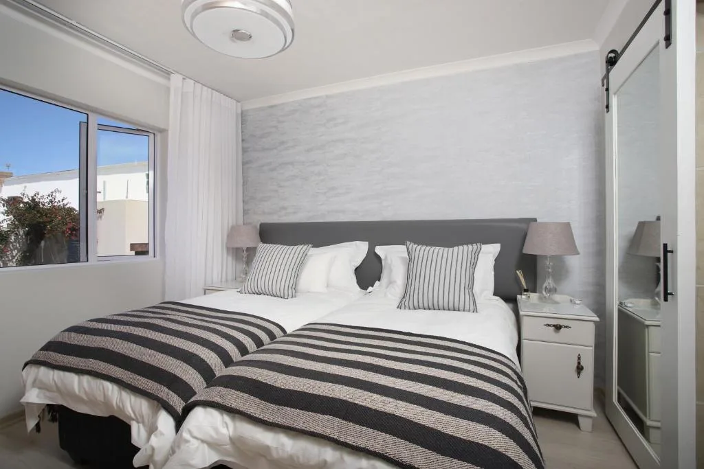 Modern bedroom with striped bedding, grey headboard, and bright windows