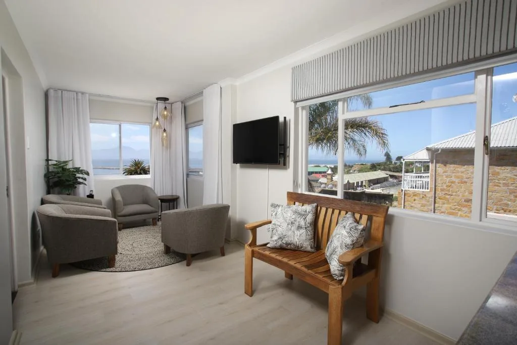 Bright lounge with gray armchairs, wooden bench, wall-mounted TV, and ocean views