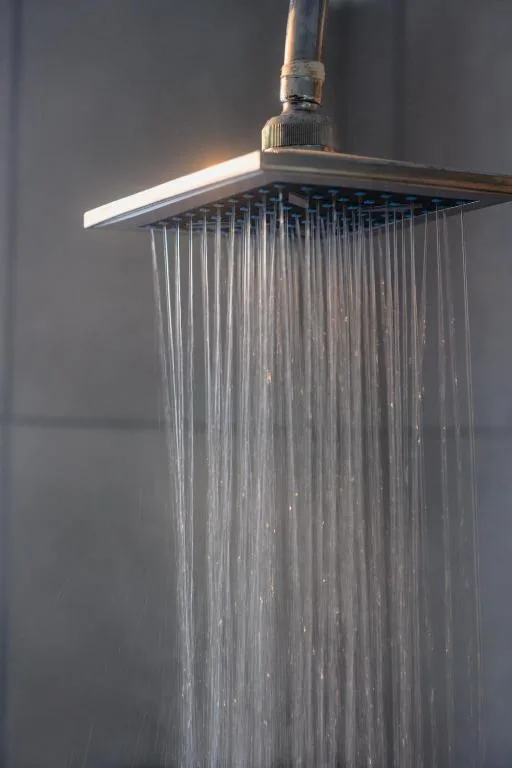 Modern rainfall showerhead with flowing water against tile wall