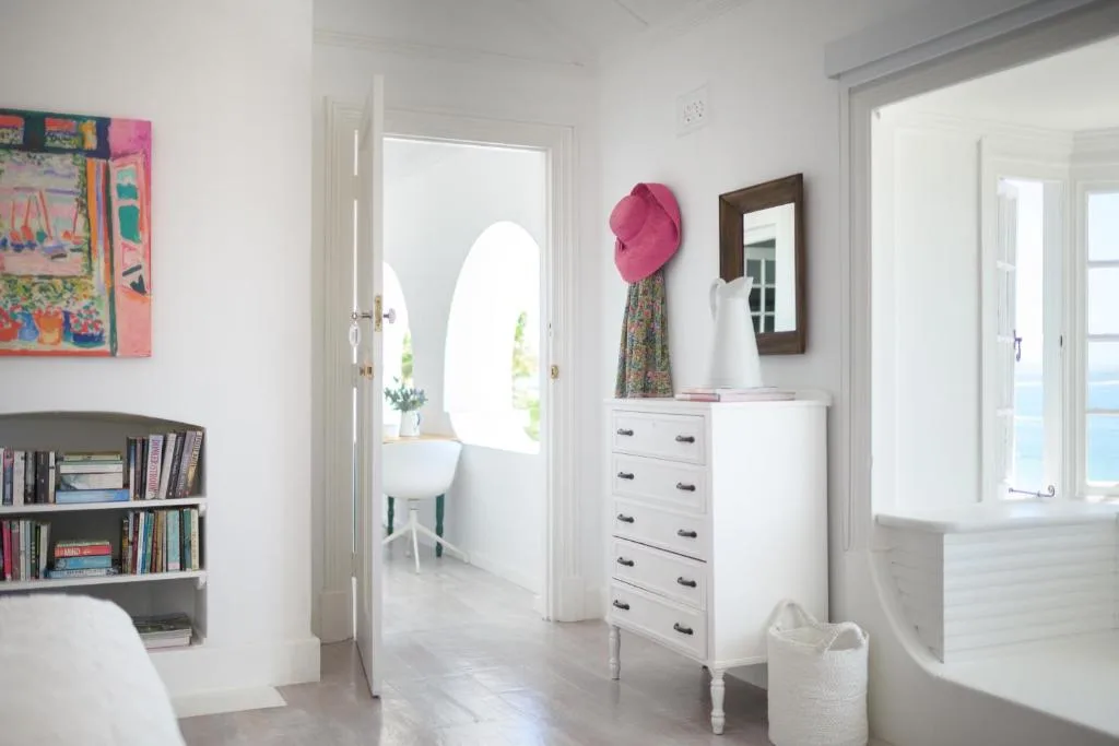 Bright bedroom with white dresser, bookshelf, colorful artwork, and ocean view