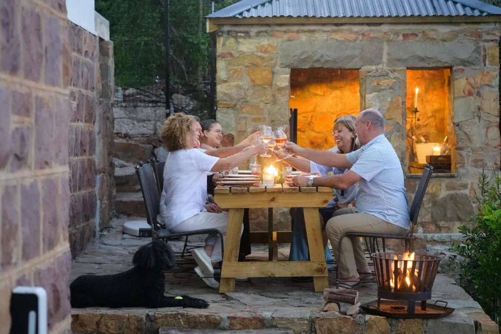 Four guests toasting wine at outdoor table on stone patio at dusk
