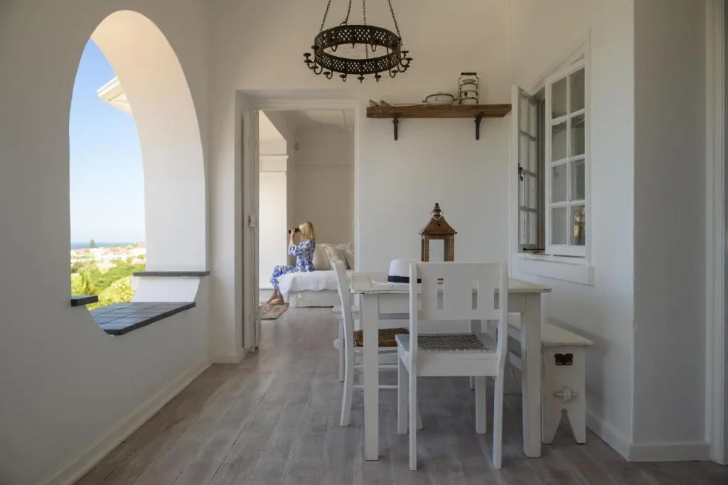 Bright dining area with white table and chairs, arched window overlooking landscape