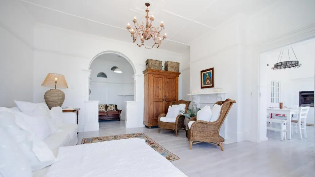 Bright white lounge with wicker chairs, bed, and elegant chandelier