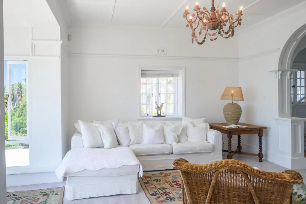Bright white lounge with cream sofa, wicker chairs, and ornate chandelier
