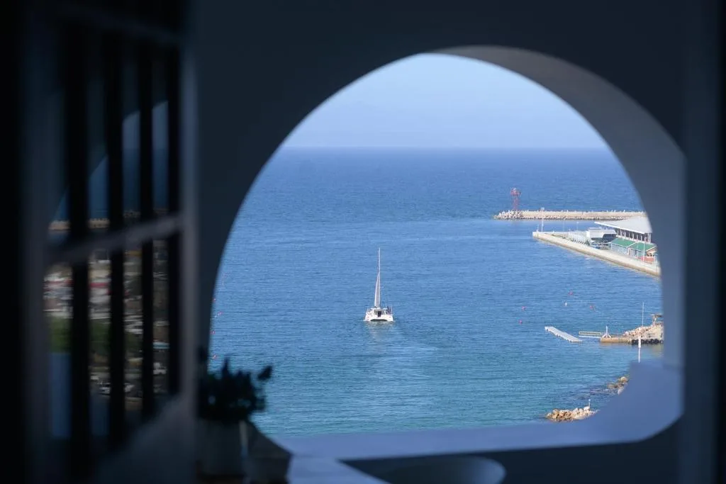 Blue ocean with sailboat and harbor viewed through rounded window opening