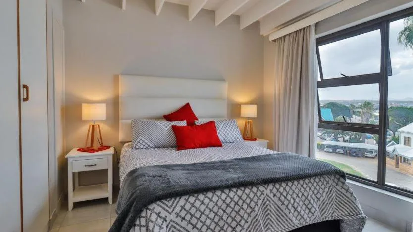 Modern bedroom with queen bed, red pillows, bedside lamps, and ocean view through large window
