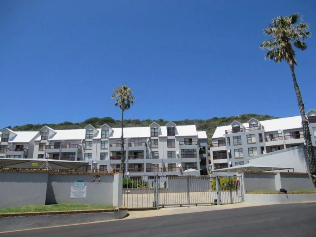 White multi-story apartment building with palm trees and gated entrance