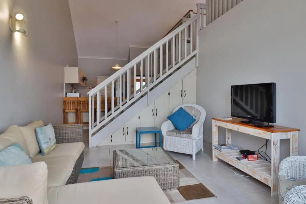 Open-plan lounge with cream sofas, TV, and white staircase to loft bedroom