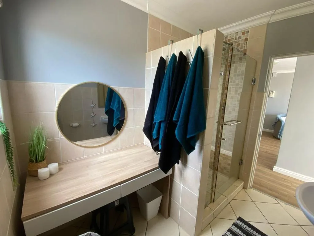 Modern bathroom with round mirror, wooden vanity, and walk-in shower enclosure