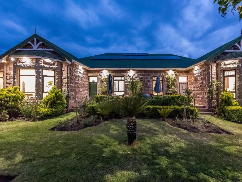Stone cottage with green roof, landscaped garden, evening lighting, Mossel Bay