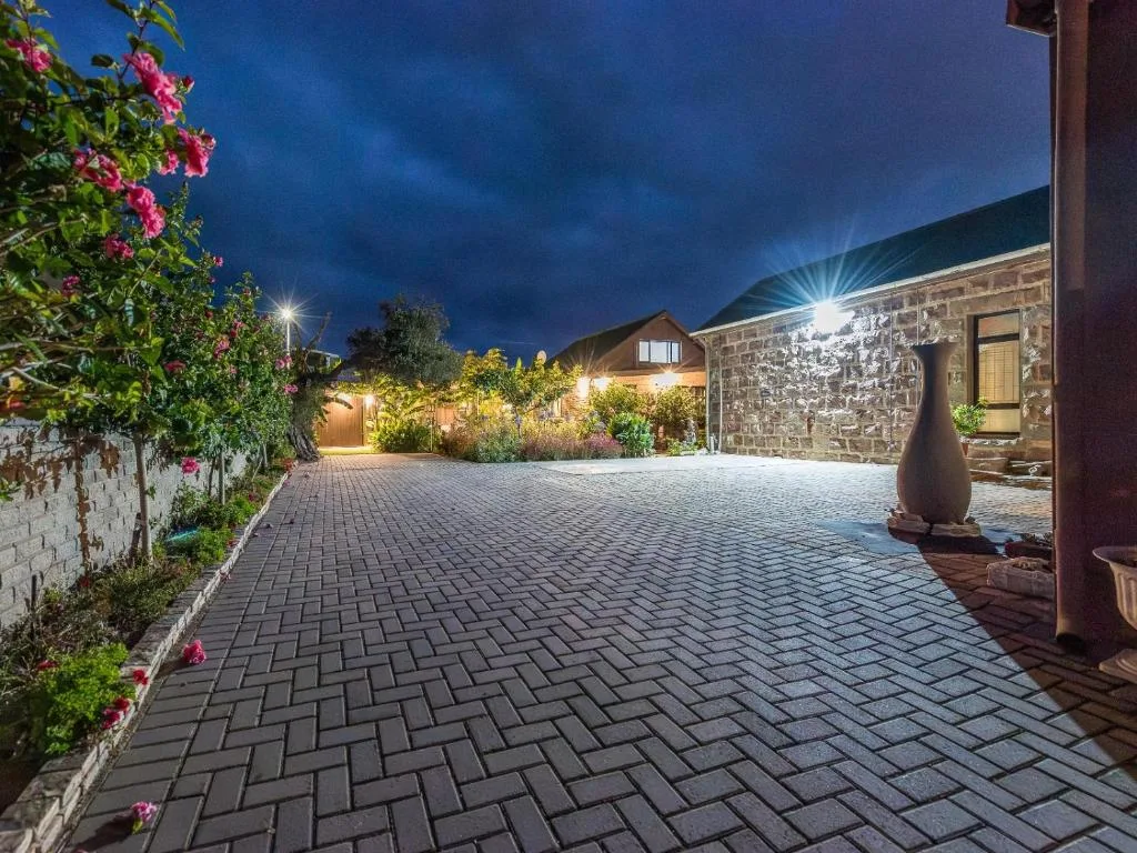 Evening view of illuminated stone cottage with paved driveway and flowering bougainvillea