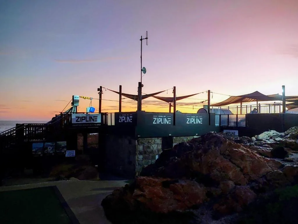 Sunset view of coastal zipline facility and rocky shoreline at dusk
