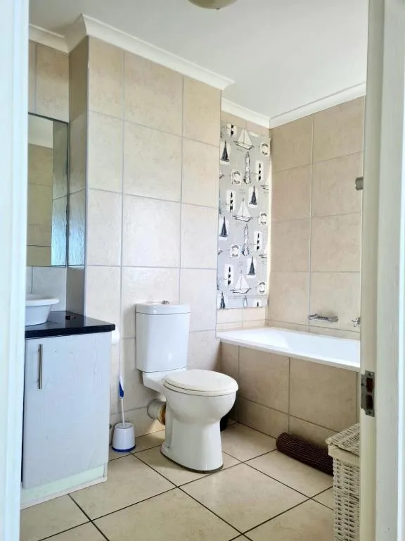 Clean bathroom with toilet, vanity, bathtub and beige tile walls