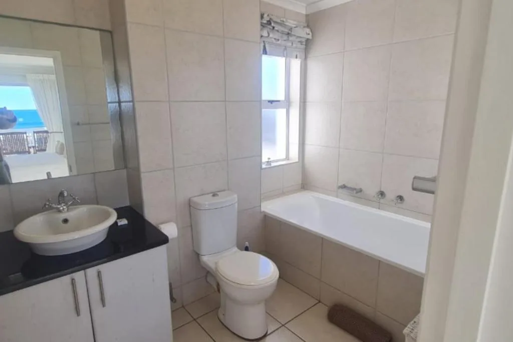 Clean bathroom with round basin sink, toilet, and white bathtub with window