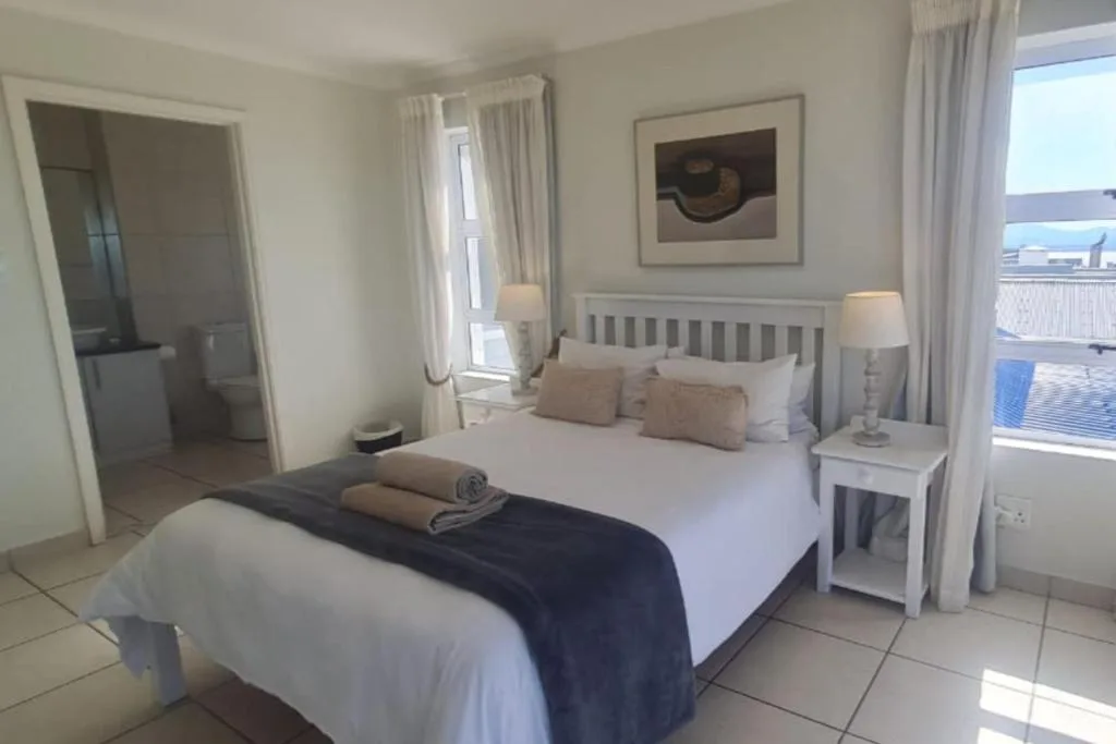 Bright bedroom with queen bed, white headboard, ocean view windows