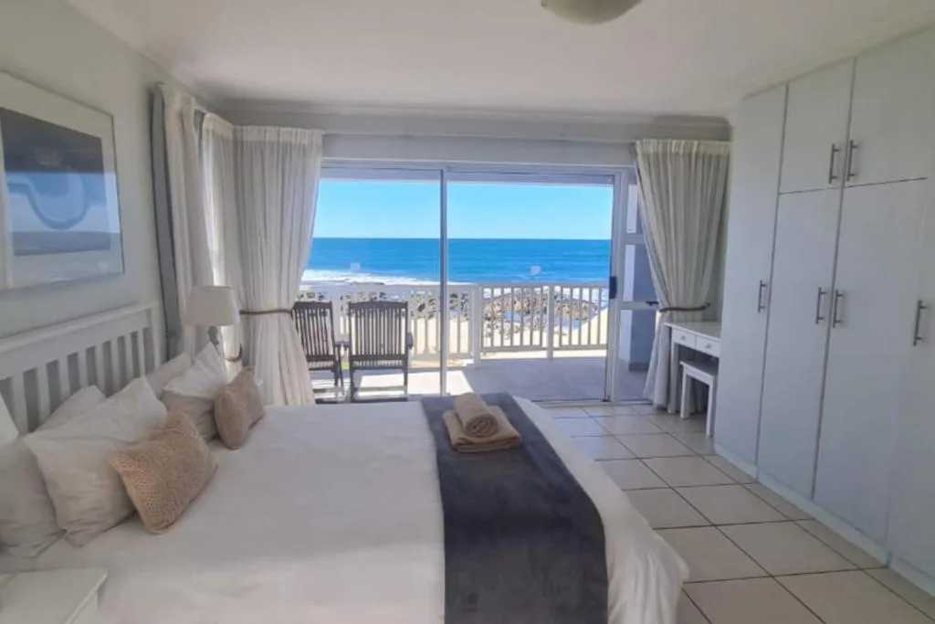 Bright beachfront bedroom with ocean view through glass doors and balcony