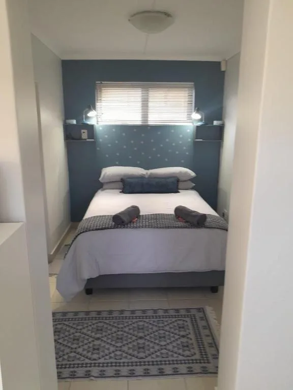 Cozy bedroom with queen bed, dark blue accent wall, and natural light from window