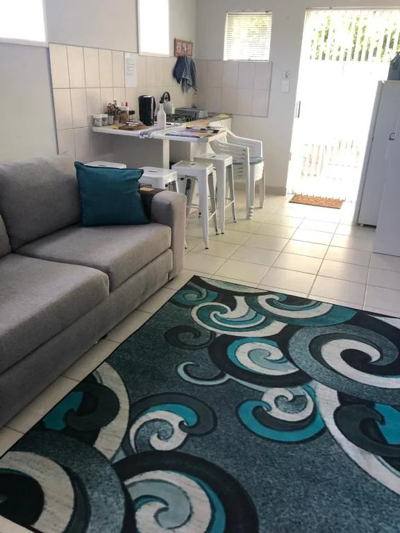 Open-plan lounge with gray sofa and patterned teal rug, leading to kitchen area