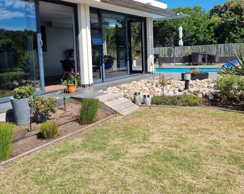 Modern home exterior with manicured gardens, pool, and patio area