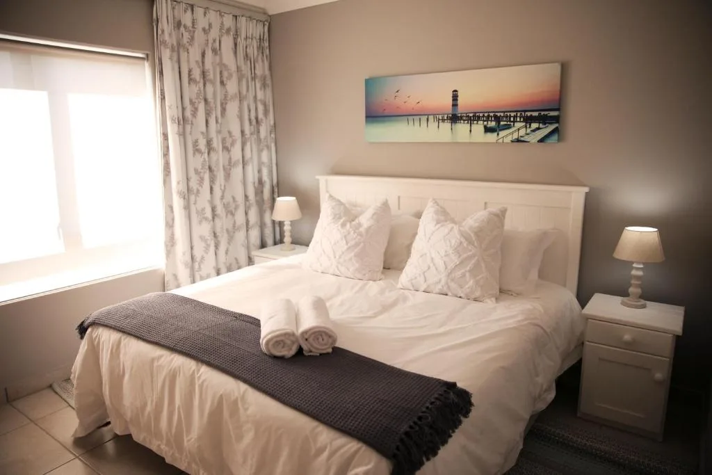 Bright bedroom with crisp white linens, patterned pillows, and rolled towels