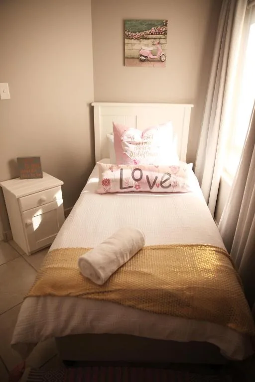 Single bed with white headboard, pink decorative pillows, and gold throw blanket