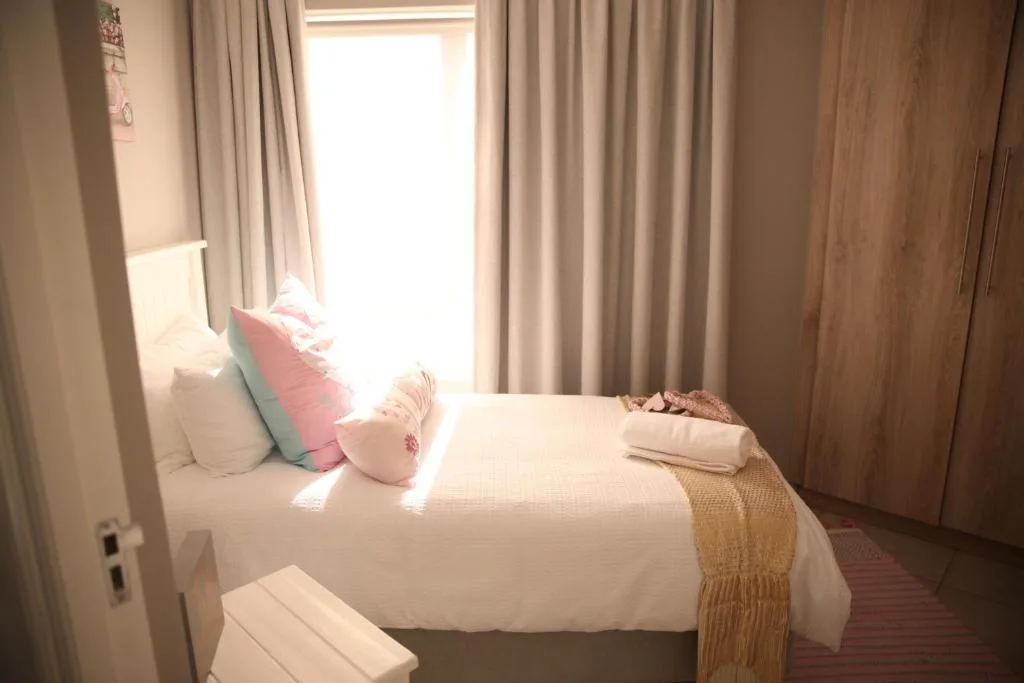Bright bedroom with white bed, colorful pillows, and natural light from door